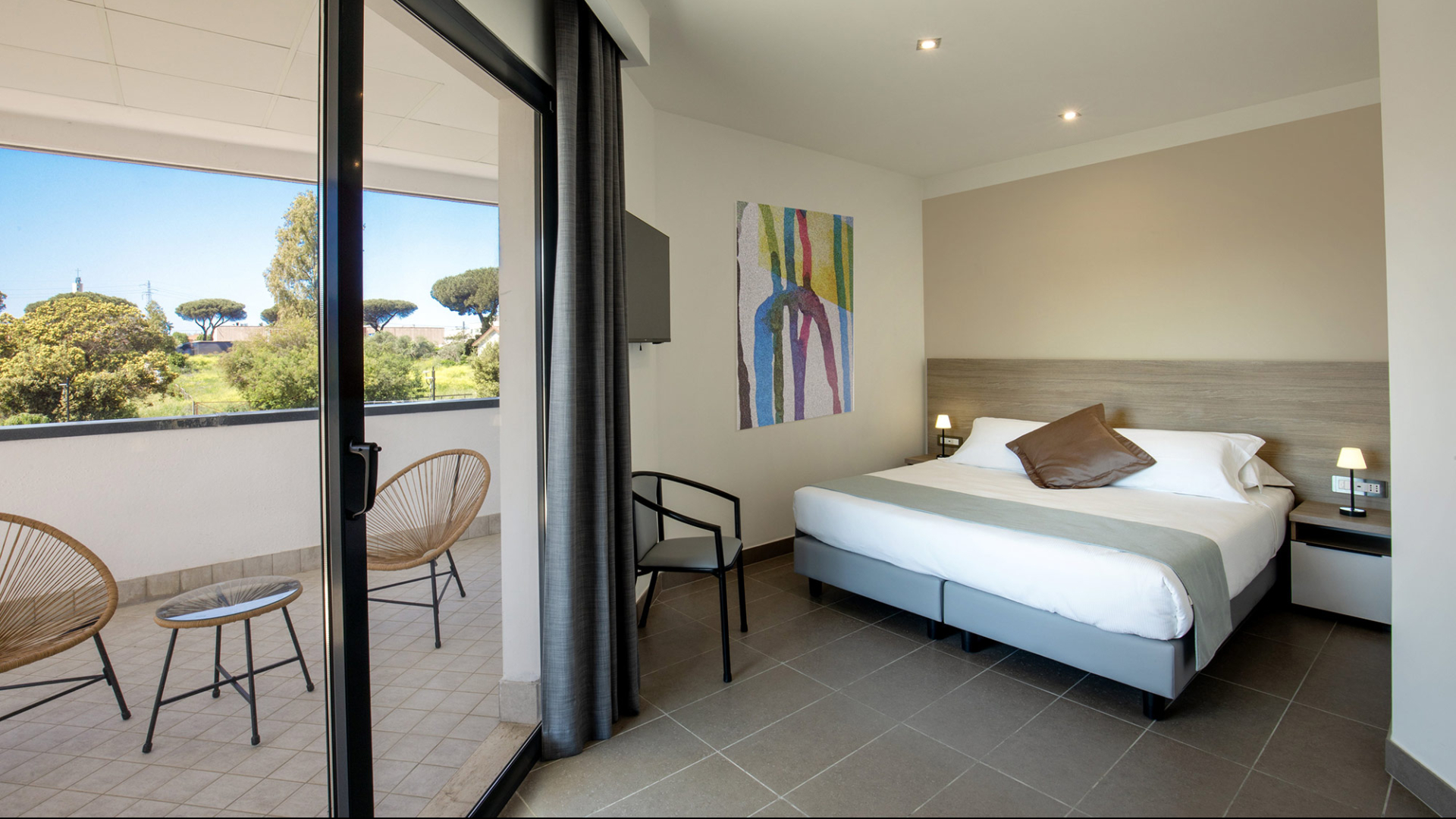 Bright room with a double bed, balcony, and view of lush trees.