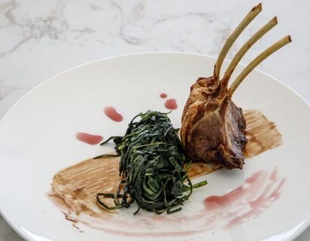 Costine d'agnello con spinaci, presentazione elegante su piatto bianco.