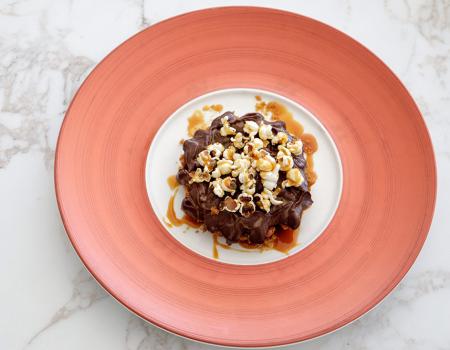 Dolce goloso con popcorn, cioccolato e caramello su piatto elegante.