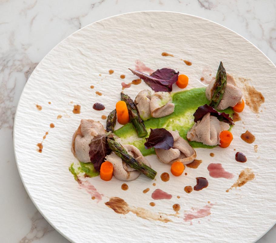 Piatto elegante con carne, asparagi, carote e salse colorate su sfondo bianco.
